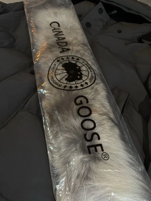 Mörkgrå pufferjacka från Canada Goose - Säljer en mörkgrå pufferjacka från Canada Goose med huva och snyggt märke på ärmen. Jackan har dragkedja och knappar framtill, två sidofickor och en clean, quiltad look. Perfekt för kalla vinterdagar och riktigt stilren.