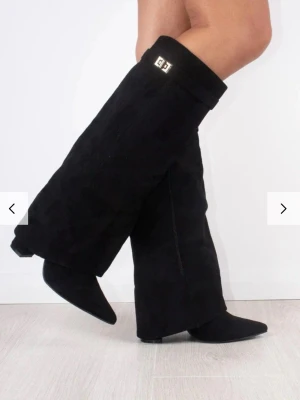 NOIR LUXE BOOTS I MOCKA-LOOK - Säljer ett par svarta stövlar i mocka med spetsig tå och låg klack. Stövlarna har en snygg guldfärgad spänndetalj upptill och en bred, rak passform som ger en cool siluett. Perfekta till kjol eller klänning för en trendig look.