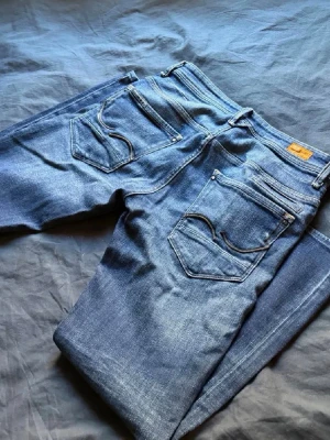 Blå jeans från Jack and Jones  - Säljer ett par klassiska blå jeans från Jack and Jones  med snygga kontrastsömmar och ikoniska bakfickor. Jeansen har normal passform och är tillverkade i slitstarkt denimtyg. Perfekta för dig som gillar tidlös stil och vill ha ett par riktigt schyssta jeans.