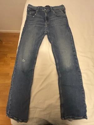 Replay jeans - Thad - Säljer ett par klassiska blå jeans från Replay med raka ben och normal passform. Jeansen har 4 fickor, samt slitningar på ena benet. Materialet är robust denim i bomull och de stängs med dragkedja och knapp. OBS lite slitna men inget farligt!