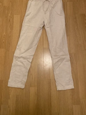  linnebyxor med snörning från H&M - Säljer ett par ljusbeige linnebyxor från H&M i storlek XS. Byxorna har elastisk midja med snörning och två sidofickor. Materialet är en linneblandning som känns luftigt och skönt. Perfekta för varmare dagar och chill stil.
