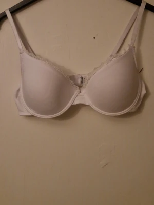 Vit bh med spets från Redcent 80C - Säljer en vit bh från Redcent i storlek 80C. Bh:n har släta kupor med dekorativ spets längs kanten och tunna axelband. Perfekt för dig som gillar enkel och stilren design med en touch av spets.