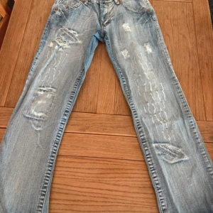 Replay ljusblå slitna jeans bootcut - Säljer ett par ljusblå jeans från Replay med slitna detaljer och råa kanter vid bensluten. Jeansen har klassisk femficksdesign, bootcut-modell och tydliga slitningar framtill och på bakfickorna. står strl M men sitter som S. 