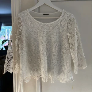 Vit spetsblus med trekvartsärm - Superfin vit blus med detaljerad spets framtill och på ärmarna. Blusen har rund halsringning, trekvartsärmar och ett vackert mönster i spetsen. Baksidan är i mjukt tyg för extra komfort. Perfekt för dig som gillar romantisk och bohemisk stil.