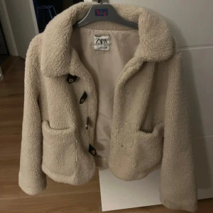  Teddyjacka från Zara, M - Supermjuk och fluffig teddyjacka från Zara. Jackan har stora fickor framtill, bred krage och stängs med snygga knappar. Perfekt för kyliga dagar när du vill vara både varm och trendig.