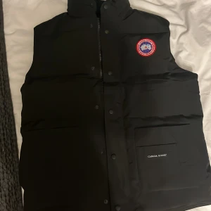Canada Goose väst – svart, i mycket bra skick - Klassisk och tidlös Canada Goose-väst i svart. Västen är i mycket bra skick, sparsamt använd och väl omhändertagen. Perfekt som ett lättare ytterplagg under höst/vår eller att ha som ett extra lager under jackan på vintern. 	•	Färg: Svart 	•	Storlek: L 	•	Mycket bra skick – inga skador, fläckar eller slitage                                                                     Nypris ca:7499kr   