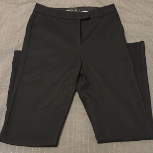 Svarta kostymbyxor från STOCKH LM - Snygga svarta kostymbyxor från STOCKH LM med klassisk rak passform och bälteshällor. Byxorna har diskreta bakfickor och en metallring som detalj vid ena hällan. Perfekta för en clean och stilren look. 