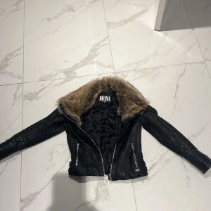 Svart skinnjacka med fuskpäls Jofama - Snygg svart skinnjacka från Jofama by Kenza i storlek 36. Jackan har en stor krage i brun fuskpäls, silvriga dragkedjor och spänndetaljer vid midjan. Perfekt för dig som vill ha en edgy och trendig look. Jackan har inga hål eller tecken på slitningar 