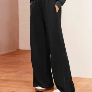 Svarta wide byxor Karl Lagerfeld - Svarta wide byxor från Karl Lagerfeld med elastisk midja och knappar längs sidorna. Byxorna har en avslappnad passform och är tillverkade i ett mjukt material som känns skönt mot huden. Perfekta för en chill och stilren look.