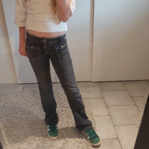 Mörkgrå bootcut jeans Gina Tricot 152 - Snygga mörkgrå jeans från Gina Tricot i storlek 152. Modellen har bootcut-ben, låg midja och coola fickdetaljer framtill med knappar. Jeansen är i klassisk denim med tydliga sömmar och passar perfekt till sneakers.💗💗 Nypris 349:-