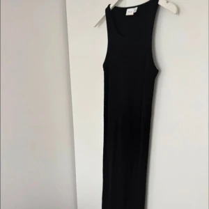 Svart lång stickad klänning från Vila - Säljer en svart lång stickad klänning från Vila. Klänningen är ärmlös med rund halsringning och har en tight passform. Perfekt för dig som gillar en enkel och stilren look med lite edge.