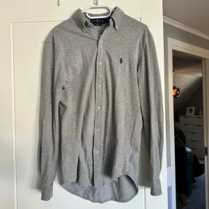 Grå skjorta från Ralph Lauren XS - Snygg grå skjorta från Ralph Lauren i featherweight mesh. Klassisk modell med knappar hela vägen, button down-krage och broderad logga på bröstet. Långärmad och i mjuk bomullskänsla, perfekt för en clean och stilren look. Storleken är XS men sitter mer som S. Pris kan diskuteras vid snabb affär