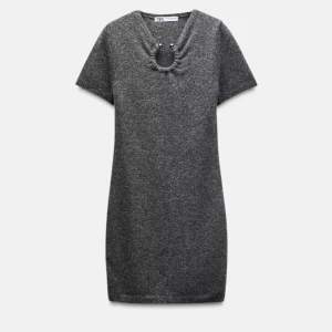 Grå stickad kortklänning från Zara - Mysig grå stickad kortklänning från Zara med korta ärmar och v-ringning. Snygg detalj med ring och pärlor vid halsen som ger en unik touch. Perfekt för dig som gillar enkel men trendig stil.