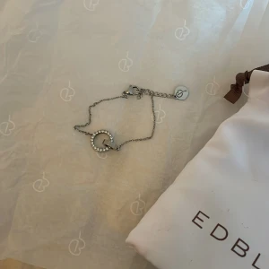 Silverarmband från Edblad med kristaller - Snyggt silverfärgat armband från Edblad med en cirkelformad berlock dekorerad med gnistrande kristaller. Tunn kedja och diskret logga vid låset. Perfekt accessoar för att lyfta din stil.