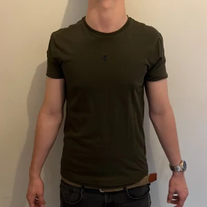 Mörkgrön t-shirt Polo Ralph Lauren - Snygg mörkgrön t-shirt från Polo Ralph Lauren i modellen Custom Slim Fit. Klassisk rund hals, korta ärmar och broderad logga på bröstet. Tillverkad i mjuk bomull som sitter skönt och har en stilren look. Modellen är 178 cm lång och väger 64 kg. Det är bara att höra av sig vid frågor och funderingar 😀