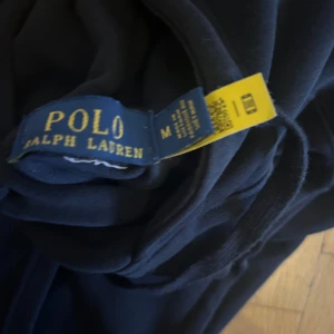 Mörkblå hoodie från Polo Ralph Lauren - Säljer en mörkblå hoodie från Polo Ralph Lauren i bomull med klassisk röd broderad logga på bröstet. Tröjan har huva med snörning, magficka och ribbade muddar. Perfekt för dig som gillar stilrena och bekväma plagg. Priset är inte hugget i sten. Går att diskutera vid en snabb affär. Ny pris 1400 passar S också !
