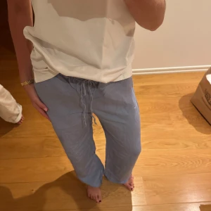 Ljusblå linnebyxor med snörning - Säljer ett par ljusblå linnebyxor från H&M med avslappnad passform och snörning i midjan. Byxorna har raka, vida ben och är perfekta för en chill och stilren look. Materialet är svalt linne och de har fickor i sidorna.