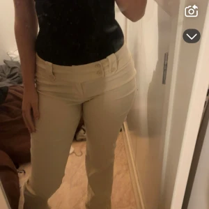 Beiga byxor med hög midja och knappar - Snygga beiga byxor med hög midja och dekorativa knappar framtill. Byxorna har en rak passform och är perfekta för dig som gillar en stilren look. Materialet känns mjukt och bekvämt, och färgen är lätt att matcha med olika toppar.