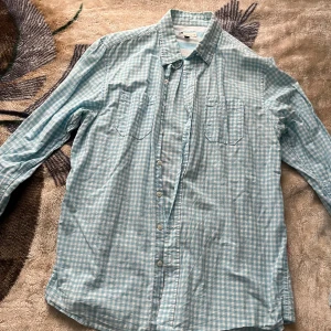 Ljusblå rutig skjorta Dressmann XL - Snygg ljusblå och vit rutig skjorta från Dressmann i storlek XL. Skjortan har klassisk krage, två bröstfickor och knäppning framtill. Tillverkad i mjuk bomull, perfekt för en chill och stilren look. Vid frågor hör av dig!