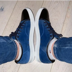 Lanvin Paris Sneaker - Snygga blå sneakers i mocka med en svart glansig captoe. Skorna har snörning och en vit sula som ger en stilren kontrast. Perfekta för en avslappnad men ändå stilfull look. Skorna passar perfekt nu till hösten och vintern och är i väldigt bra skick. Hör av dig vid minsta lilla fundering. Skorna är i uk10 vilket motsvarar ungefär 44-45