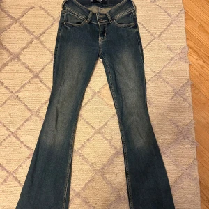 Blå bootcut jeans från Hollister - Snygga blå bootcut jeans från Hollister med coola broderade detaljer på bakfickorna. Jeansen har låg midja och är tillverkade i mjukt denim med lätt stretch. Midjemått:31cm Innerbenslängd:81cm