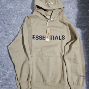 Priset diskuteras Beige hoodie från Essentials - Säljer en snygg beige hoodie från Essentials med svart text på framsidan. Hoodien har en klassisk design med en stor ficka framtill och ribbade muddar. Perfekt för streetwhere stil. 