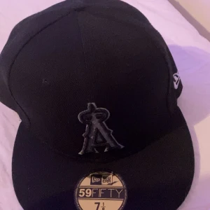 Svart New Era 59FIFTY keps - Säljer en svart fitted keps från New Era, modell 59FIFTY. Kepsen har broderad logga framtill och MLB-logga bak. Klassisk rak skärm och broderad New Era-logga på sidan. Tillverkad i bomull och polyester för en skön passform.