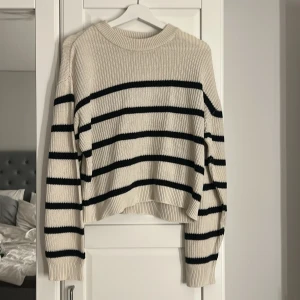 Randig stickad tröja från H&M - Beige stickad tröja från H&M med svarta horisontella ränder. Tröjan har en rund halsringning, ribbade muddar och lång ärm. Perfekt för lager-på-lager och chill höst- eller vårstil.
