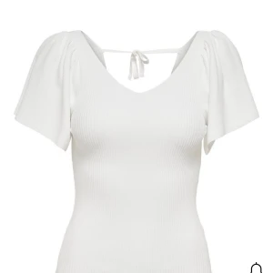 Vit ribbad topp med knyt från ONLY - Supersöt vit ribbad topp från ONLY med v-ringning, korta vida ärmar och knyt i ryggen. Toppen har en figurnära passform och är tillverkad i mjuk bomullsmix. Perfekt för dig som gillar en enkel men ändå trendig look. Säljer en likadan i svart!❣️