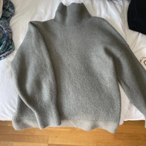 Grå grön polotröja i ullmix XS - Mysig grå/grön polotröja i ullblandning med hög krage och lång ärm. Tröjan har en loose passform och är perfekt för kyliga dagar. Enkel och stilren design som funkar till många outfits.