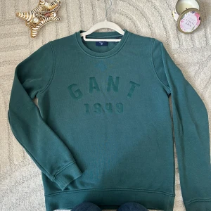 Grön sweatshirt från GANT - Snygg grön sweatshirt från GANT med broderad logga och årtalet 1949 framtill. Tröjan har rund halsringning, långa ärmar och ribbade muddar vid ärmslut och nederkant. Perfekt för en chill och stilren look.