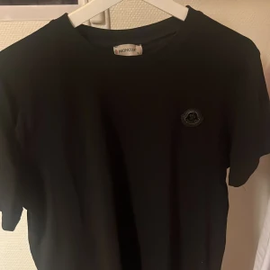 Moncler t-shirt  - Svart t-shirt från Moncler i klassisk modell med rund hals och korta ärmar. Diskret Moncler-logga i svart på bröstet. Tillverkad i mjuk bomull som känns skön mot huden. Perfekt för en clean och stilren look.