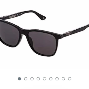 Svarta solglasögon från Police - Snygga svarta solglasögon från Police med klassisk rektangulär form och mörka glas. Bågarna har en diskret textur och silverdetaljer vid gångjärnen samt Police-logga på sidan. Perfekt accessoar för en cool look. Glasögonen har samma form som på första bilden men märket ser annorlunda ut på sidan.