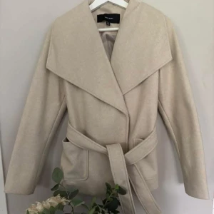 Beige omlottjacka med bälte Vero Moda - Snygg beige jacka från Vero Moda med bred krage och omlottstängning. Jackan har ett matchande bälte i midjan och två fickor framtill. Perfekt för dig som gillar stilrena och trendiga plagg. Jackan är i strl xs men blev förstor för mig , skulle tro även en small kan ha denna därav har den blivit använd endast 1 tillfälle å sedan hängt i garderoben efter 