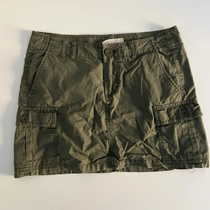 Olivgrön cargokjol lågmidjad från H&M L.O.G.G. - Olivgrön lågmidjad cargokjol. Kjolen är kort och har bälteshällor. Tillverkad i bomull. Strl 36, passar en S med ca. 25 i midja.