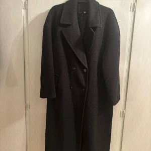 Svart lång kappa från 157, XL - Stilren svart kappa från 157 i storlek XL. Lång modell med breda slag, dubbelknäppning och fickor på sidorna. Perfekt för dig som gillar en klassisk och oversized look. Fodrad insida för extra komfort.