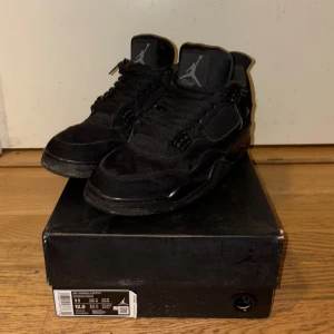 Nike Air Jordan 4 Retro Black Cat - Säljer ett par Nike Air Jordan 4 Retro Black Cat i helsvart mocka och mesh. Ikonisk Jumpman-logga på plös och häl, klassisk siluett med snörning och robust sula. Perfekta för dig som gillar streetwear och vill sticka ut med en tidlös sneaker.