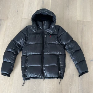 Ralph Lauren Jacka - Säljes: Ralph Lauren Dunjacka – Svart, Storlek S  Snygg och varm dunjacka från Ralph Lauren i klassisk svart färg. Jackan är i mycket bra skick och knappt använd – inga skador, fläckar eller slitage. ♦️Storlek: S ♦️Färg: Svart ♦️Skick: Mycket bra ♦️Detaljer: Ikonisk röd Ralph Lauren-logga på bröstet Två ytterfickor med dragkedja Innerficka med dragkedja Justerbar nederkant med dragsko Varmt och vadderat material – perfekt för vintern Huva för extra skydd mot kyla och vind