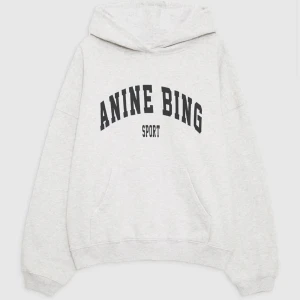 Grå hoodie från Anine Bing  - Säljer en ljusgrå hoodie från Anine Bing med svart tryck framtill. Köpt på NK. Oversized passform, stor huva och känguruficka. Mjuk bomullsblandning och ribbade muddar vid ärmslut och nederkant. Använt fåtal gånger. Är i strl S. Nypris 2700kr