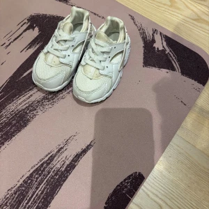 Vita Nike sneakers för barn - Säljer ett par vita Nike sneakers för barn med cool design och detaljer i mesh och syntet. Skorna har snörning och en chunky sula som ger en sportig vibe. Perfekta för dig som gillar streetstyle och vill ha något bekvämt och snyggt på fötterna.