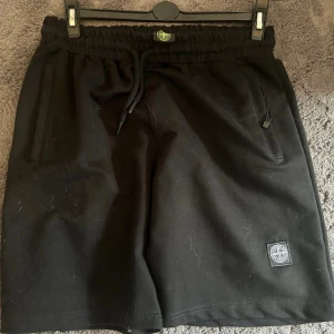Svarta shorts från Stone Island - Svarta shorts från Stone Island med elastisk midja och snörning. Klassisk logopatch på vänster ben. 