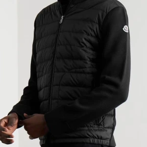 Svart quiltad cardigan jacka Moncler - Svart cardigan jacka från Moncler med quiltad framsida och stickade ärmar. Jackan har dragkedja framtill, hög krage och Moncler-logga på ärmen. Perfekt för lager-på-lager och stilren look. FINNS I FLERA STORLEKAR 