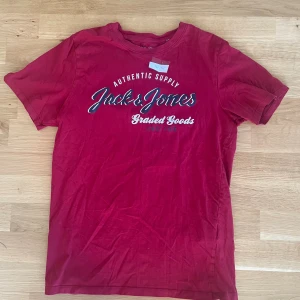 Röd Jack & Jones t-shirt med tryck - Snygg röd t-shirt från Jack & Jones med coolt vitt och blått tryck på bröstet. Klassisk rund hals och korta ärmar. Perfekt för en avslappnad stil. Gjord i mjuk bomull som känns skön mot huden.