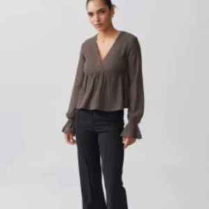 Brun blus med v-ringning - Supersöt brun blus med v-ringning och volang nedtill. Långa ärmar med lätt utsvängda ärmslut ger en chill och trendig vibe. Perfekt till svarta byxor eller jeans för en snygg look.