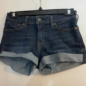 Mörkblå jeansshorts från Crocker XS - Snygga mörkblå jeansshorts från Crocker i modellen Pep! Skinny. Klassisk femficksdesign, uppvikta benslut och tydliga kontrastsömmar. Perfekta för sommaren och lätta att matcha med allt. Stilsäker och tidlös denim-look.