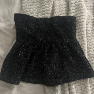 Glittrig svart tubtopp från Gina Tricot - Säljer en svart glittrig tubtopp från Gina Tricot i storlek XS. Toppen är bandeau-modell och har en fluffig, lite utställd form. Perfekt för dig som vill sticka ut med en snygg och festlig look. Materialet är syntet och toppen är axelbandslös.