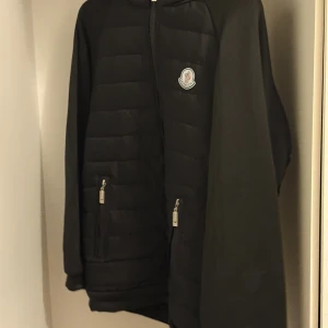Svart quiltad jacka från Moncler - Svart quiltad jacka från Moncler med dragkedja framtill och två fickor med dragkedja. Jackan har en stilren look med Moncler-logga på bröstet och är tillverkad i syntetmaterial. Perfekt för dig som gillar en clean och sportig stil.