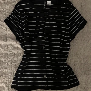 Svartvit randig topp med knappar - Svart topp från H&M med vita horisontella ränder och knappar hela vägen framtill. Kortärmad och med rund halsringning. Perfekt för en avslappnad och trendig look.