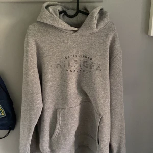 Grå hoodie från Tommy Hilfiger - Säljer en grå hoodie från Tommy Hilfiger med broderad logga på bröstet. Tröjan har huva, magficka och långa armar. Skriv vid funderingar!