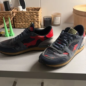 Valentino Rockrunner sneakers camo - Snygga Valentino Rockrunner sneakers med coolt kamouflagemönster i blått, rött och grått. Skorna har detaljer i mocka och skinn, samt nitar på hälen. Klassisk snörning och platt sula. Perfekta för hösten och vintern.